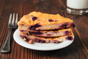 Pie with currants on a white plate, fork and glass of milk on a