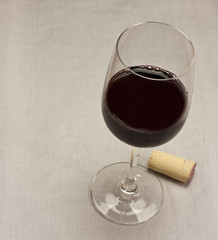 Glass of red wine with cork, on grey textile texture