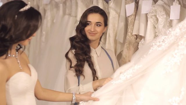 The consultant helps the girl to choose a wedding dress