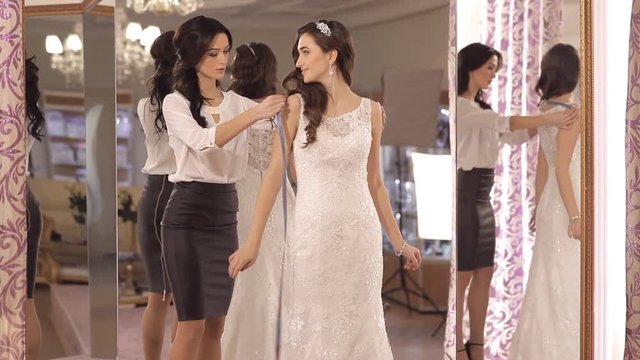 The consultant helps the girl to choose a wedding dress