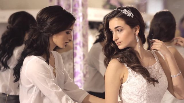 The consultant helps the girl to choose a wedding dress