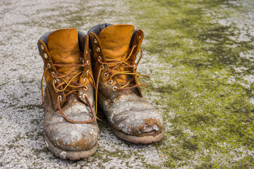 Old worn work boots on grungy dirty ground background