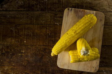Single and half fresh corn on chopping block and the wood table.