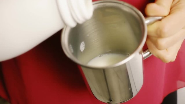Pouring fresh white milk in a tin cup.