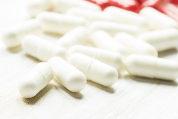 Fototapeta na wymiar White pills in capsules on a white wooden background, not isolat