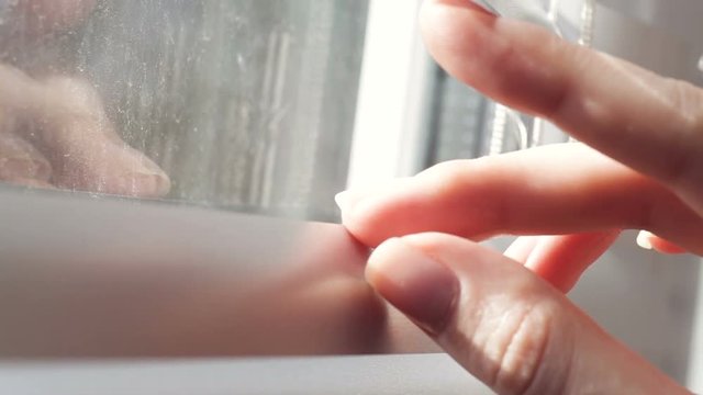 Female hand separating slats of venetian blinds with a finger to see through