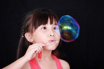 Happy girl play with soap bubbles isolated black background