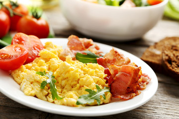 Scrambled eggs with bacon and vegetables on a grey wooden table