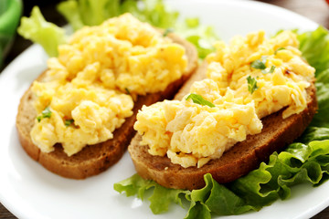 Scrambled eggs with bread and vegetables on a grey wooden table