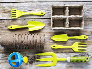 Garden tools and cardboard pots on wooden plank background
