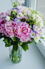 Rich bunch of pink peonies peony and lilac eustoma roses flowers in glass vase on white background. Rustic style, still life. 