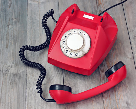 Red rotary telephone off hook on a wooden platform.