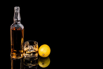 Bottle and glass whiskey and  lemon on black background