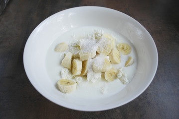 Fresh cottage cheese, banana slices, sugar and milk / yogurt are in a white dish. Ingredients for dough for cheesecakes. Preparation for cooking. 