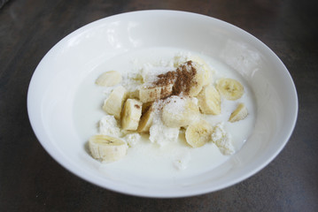 Fresh cottage cheese, banana slices, sugar, cinnamon and milk / yogurt are in a white dish. Ingredients for dough for cheesecakes. Preparation for cooking. 