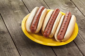 three grilled hotdog with buns in yellow plate