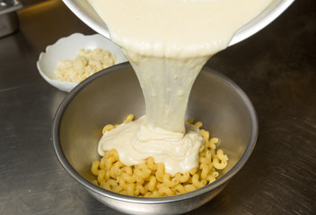 Melted cheese being poured onto cooked Macaroni pasta.