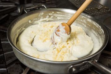 Cheese being mixed into a hot pan, to melt in preparation for Macaroni cheese