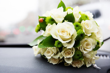 Bridal bouquet of white roses next to car windshield on the dashboard. Traffic jam on background