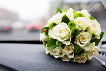 Bridal bouquet of white roses next to car windshield on the dashboard. Traffic jam on background