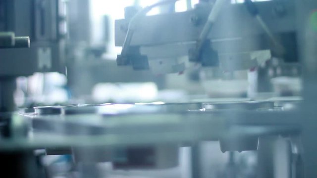 Packing machine/Food packing process at modern factory/Packaging line at dairy factory/Plastic containers on packaging line at food factory/Industrial equipment at dairy plant/Labeling package