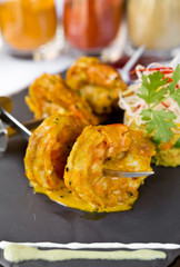 Curried King Prawns on metal skewers, served on a slate plate, with dry chilli and yoghurt.