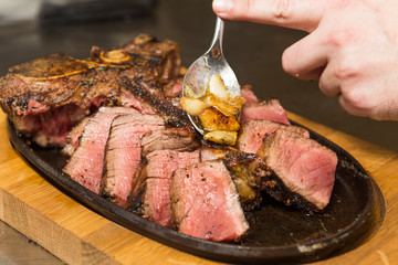A selection of grilledT Bone steak pieces and roasted garlic, off the bone on a metal plate