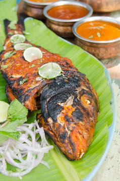 Grilled spicy fish tikka served with mint, lime, sauces and a banana leaf in a rustic setting.