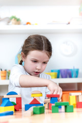 cute girl plays with toy building blocks at kindergarten