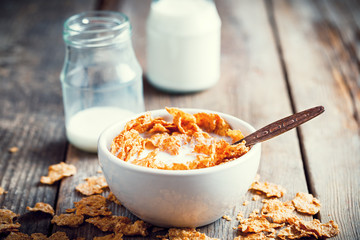 Breakfast cereal wheat flakes in bowl and milk bottles on wooden
