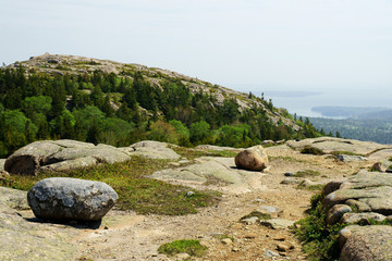 A view from high elevation over the mountain peak with water and white haze on the distance.