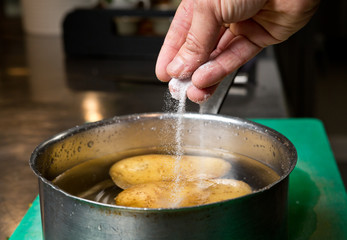 Salt being dropped into a pan of hot water containing potatoes