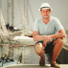 Handsome fashion man on pier in port with yachts.