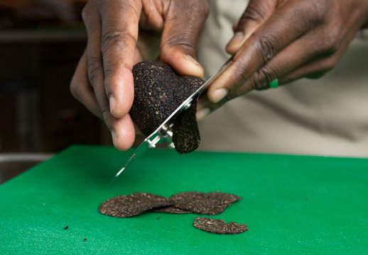 Expensive gourmet Black truffle being sliced thinly on a green cutting board