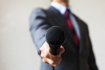 Man in business suit holding a microphone conducting a business interview, journalist reporting, public speaking, press conference, MC