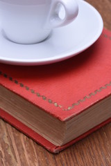 Cup of coffee and book on wooden table closeup