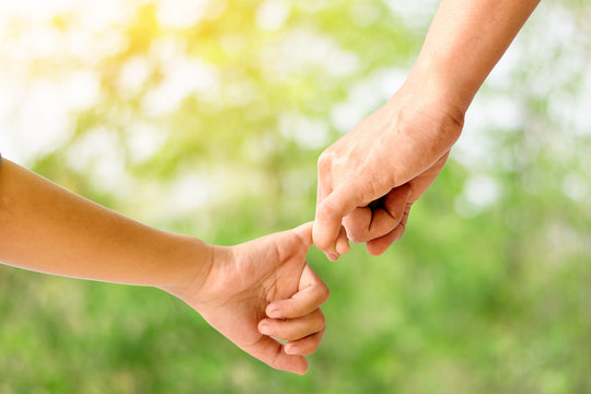Closeup of mother holding her  children hand on beautiful green nature background.