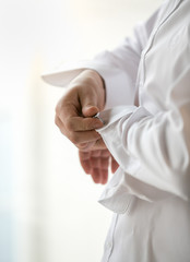 Closeup of stylish man in white shirt putting on cufflinks