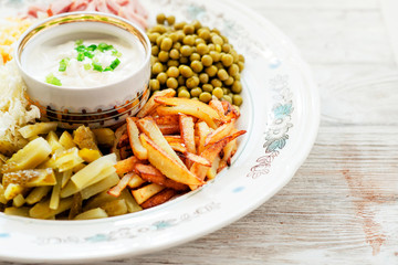 
salad with lots of ingredients - roasted potatoes, green peas , boiled eggs , ham , cabbage , pickled cucumbers , green onions , and mayonnaise on a wooden background 