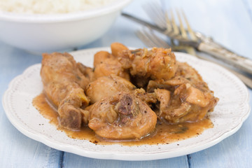 boiled chicken with beer sauce in white plate and rice in bowl on blue background