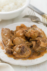 boiled chicken with beer sauce in white plate and rice in bowl on white wooden background