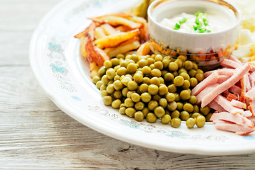 
salad with lots of ingredients - roasted potatoes, green peas , boiled eggs , ham , cabbage , pickled cucumbers , green onions , and mayonnaise on a wooden background 