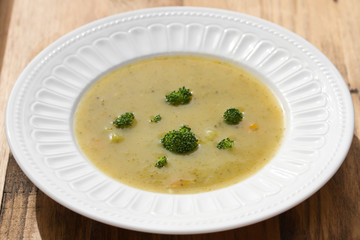 vegetable soup with broccoli on white dish on brown wooden background