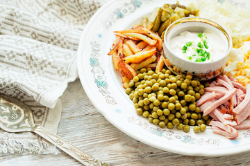 
salad with lots of ingredients - roasted potatoes, green peas , boiled eggs , ham , cabbage , pickled cucumbers , green onions , and mayonnaise on a wooden background 
