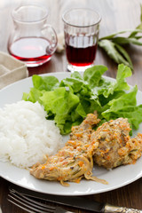 rabbit with boiled rice and salad on white plate on brown wooden background