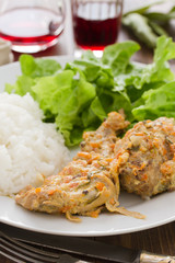 rabbit with sauce,  boiled rice and salad on plate and red wine