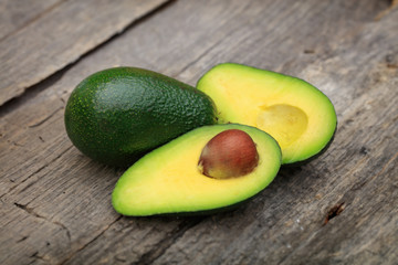 Two avocados one cut in two with seed, on wooden surface