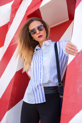 Fashion  girl posing over Red white striped wall background. Beauty woman with pink lips make-up posing on the street. 