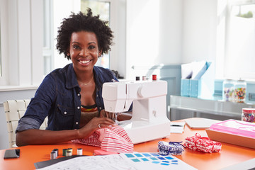 Young black woman using a sewing machine looking to camera