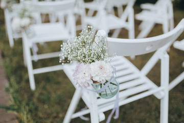 composition from flowers and herbs hanging on a white chair in the wedding ceremony area